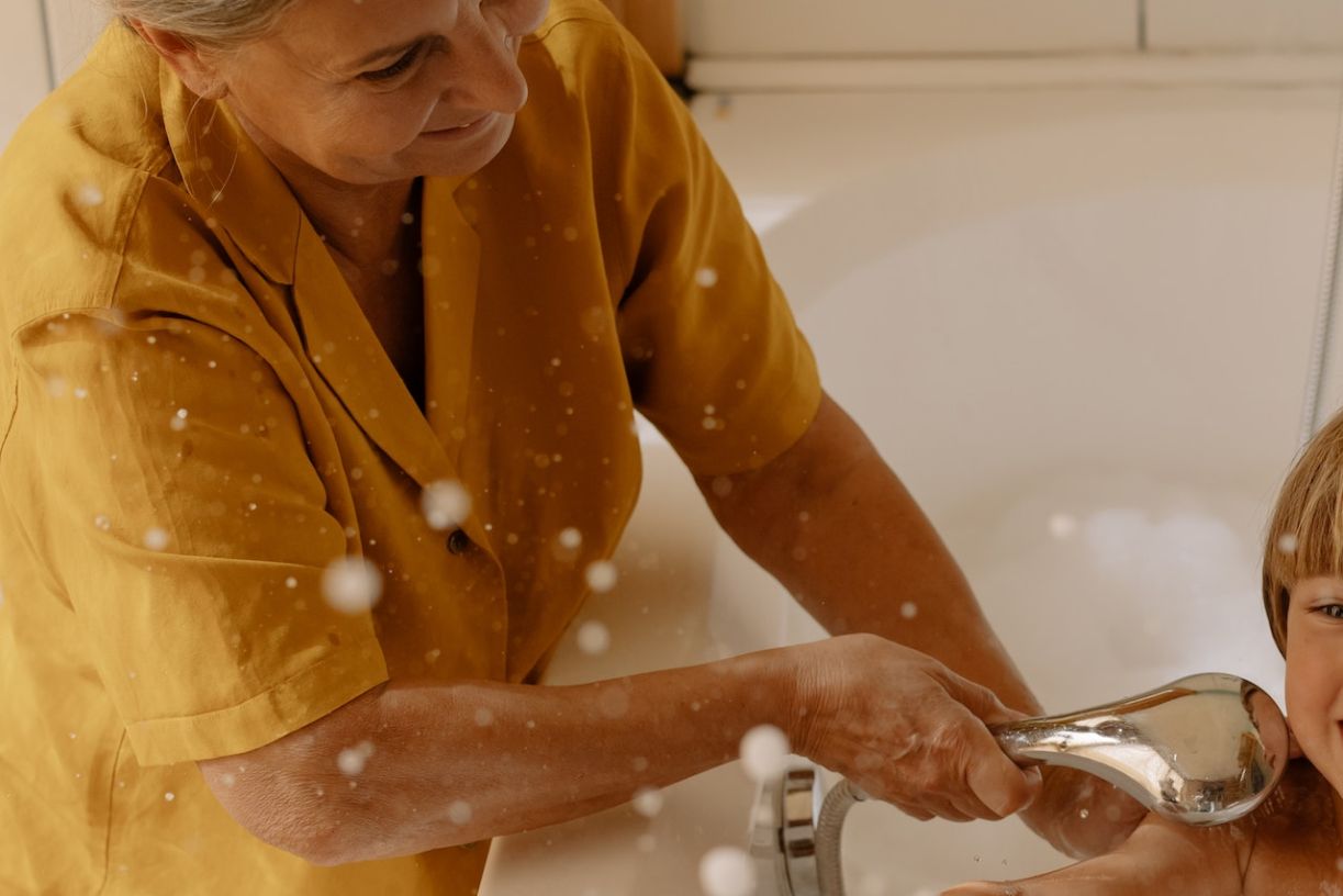 Elderly woman washing grandchild in wide bathroom